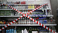 Shelves Full of Bottles of Alcoholic Beverages With Red and White Tape Blocking Shelves in Shape of Large X