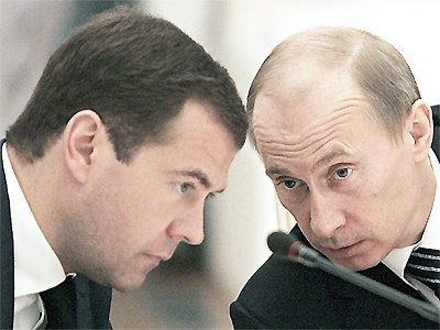 File Photo of Dmitri Medvedev and Vladimir Putin with Heads Bowed Over Microphone